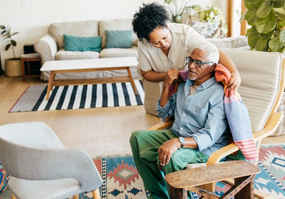 Caregiver assisting elderly man with blanket.